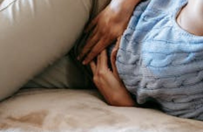 Crop anonymous female in casual outfit writhing on sofa while having stomach ache