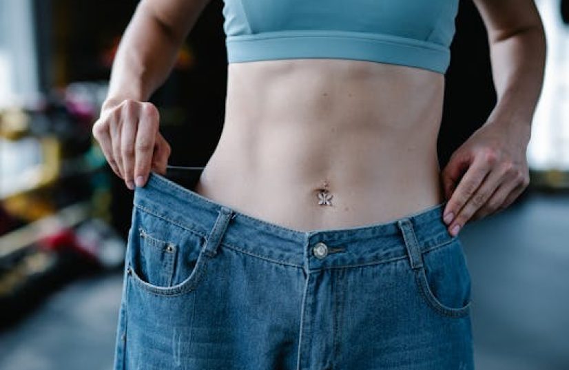 A woman shows her weight loss by holding oversized jeans revealing her toned stomach.
